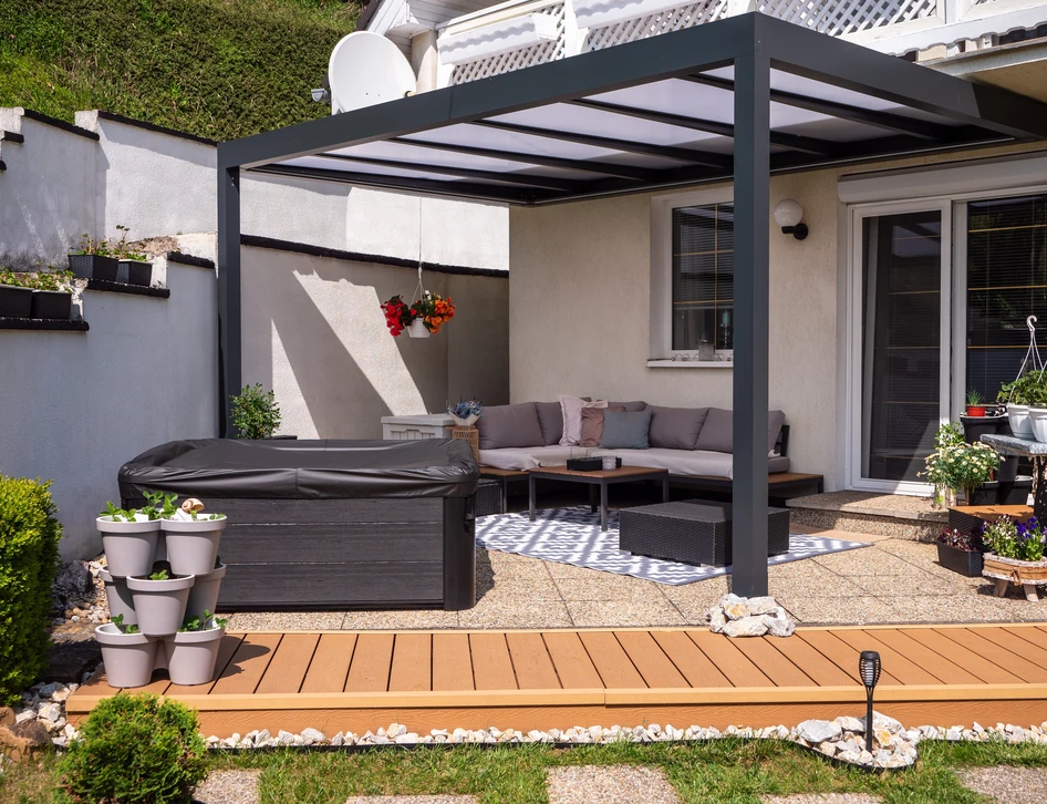 Pergola moderne en aluminium sur le patio arrière avec des sièges extérieurs, bain à remous et plantes décoratives dans un jardin résidentiel